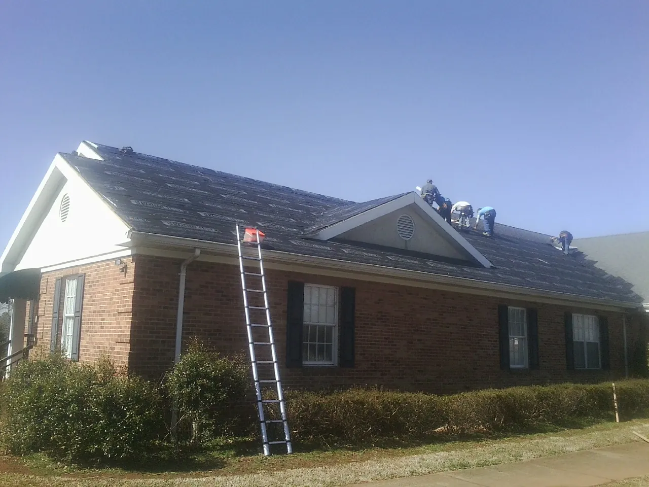 Crew tearing shingles off a brick ranch roof with a ladder set — Metal Roof Repair work by our crew in Shermans Dale