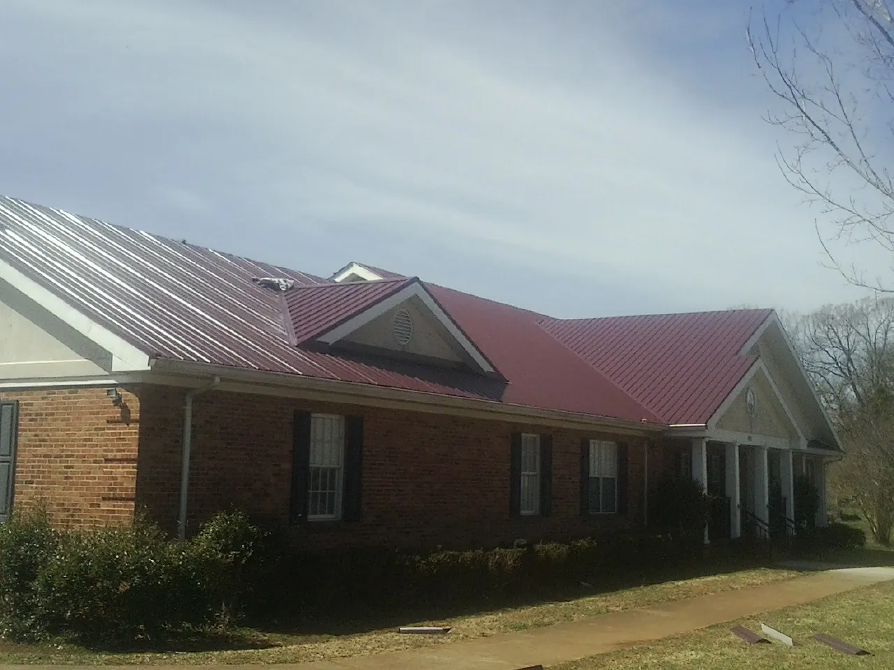 Red metal roof with gabled entries on a long brick building, from a Hail Damage Roof Repair job in Shermans Dale