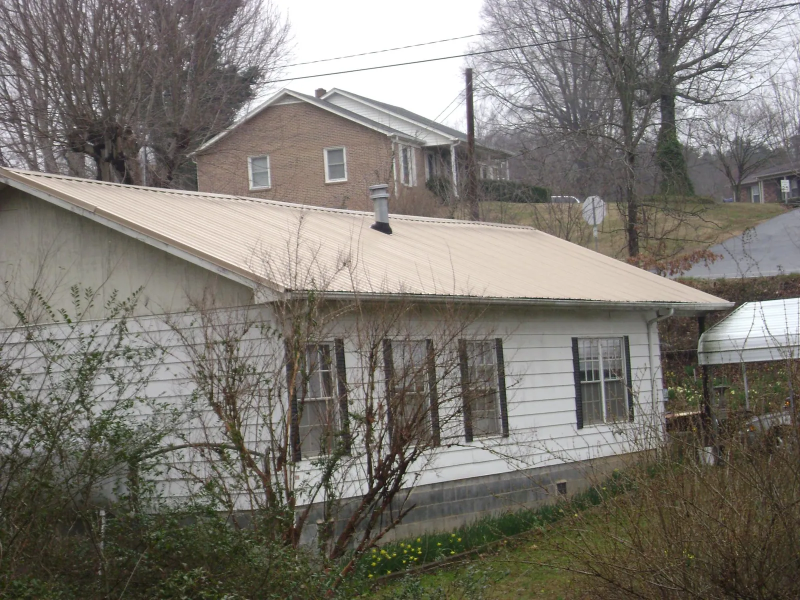Tan metal roof on a white sided house set into a hillside — Commercial Roofing by Roofing Brothers in Shermans Dale