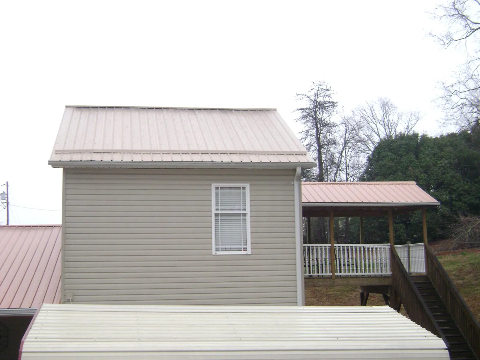 Tan metal roofs on a two story addition and attached porch, from a Roof Replacement job in Shermans Dale